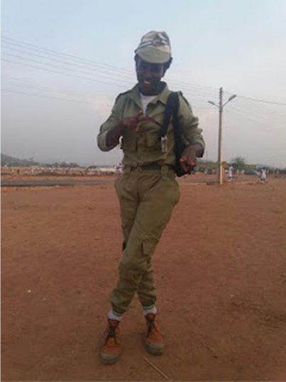 Peace Itimi wearing her NYSC uniform with her legs crossed smiling at the camera
